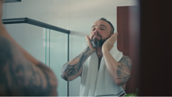 A man patting his face post-wash, preparing for the disciplined application of beard oil as part of his grooming ritual.